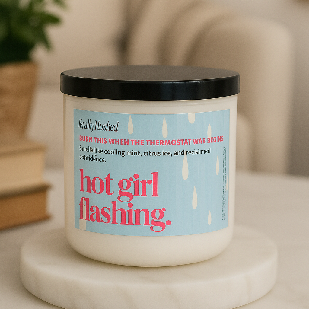 Candle with a label on a marble surface, with a plant and books in the background.