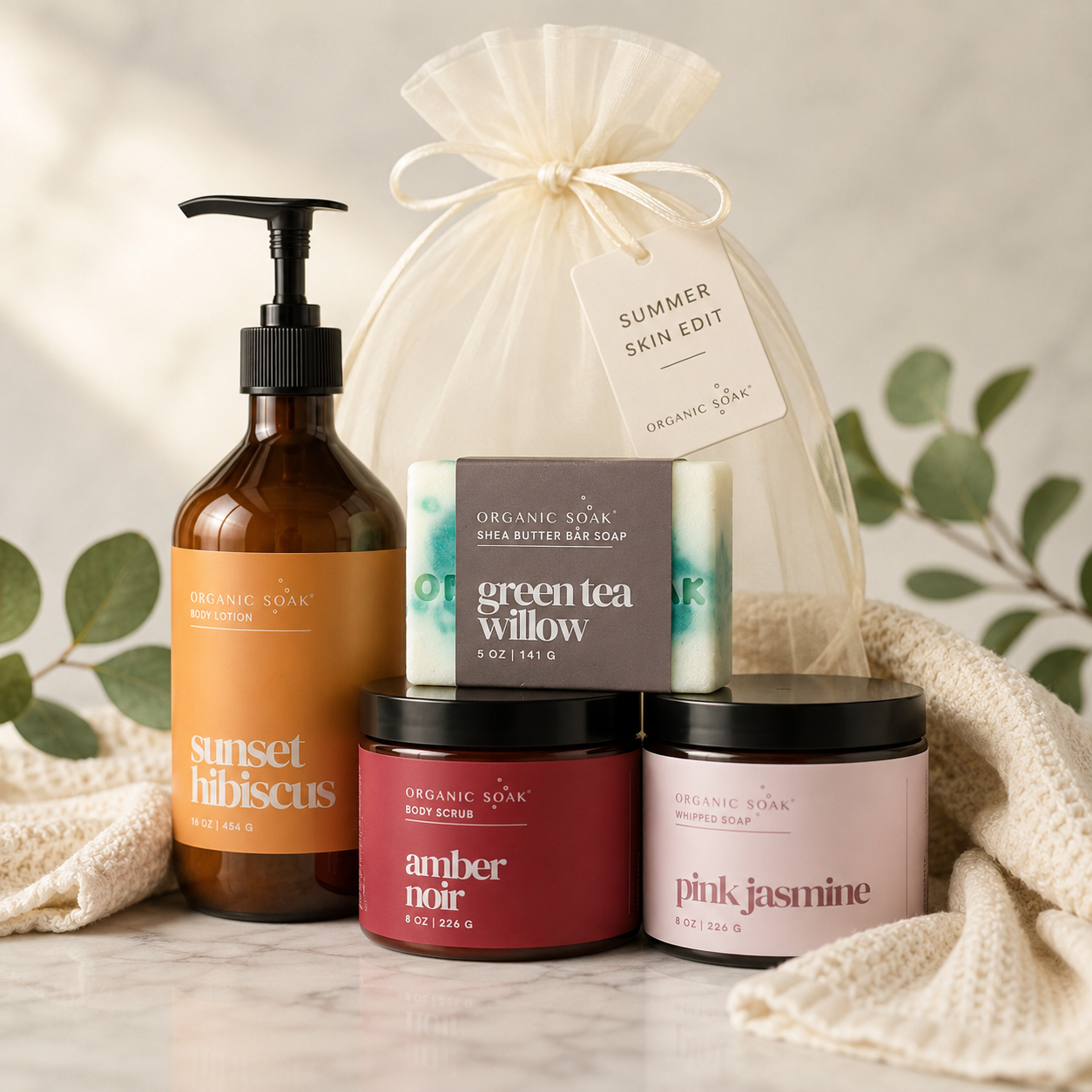 Collection of organic skincare products including a bottle, soap, scrub, and candle on a neutral background.
