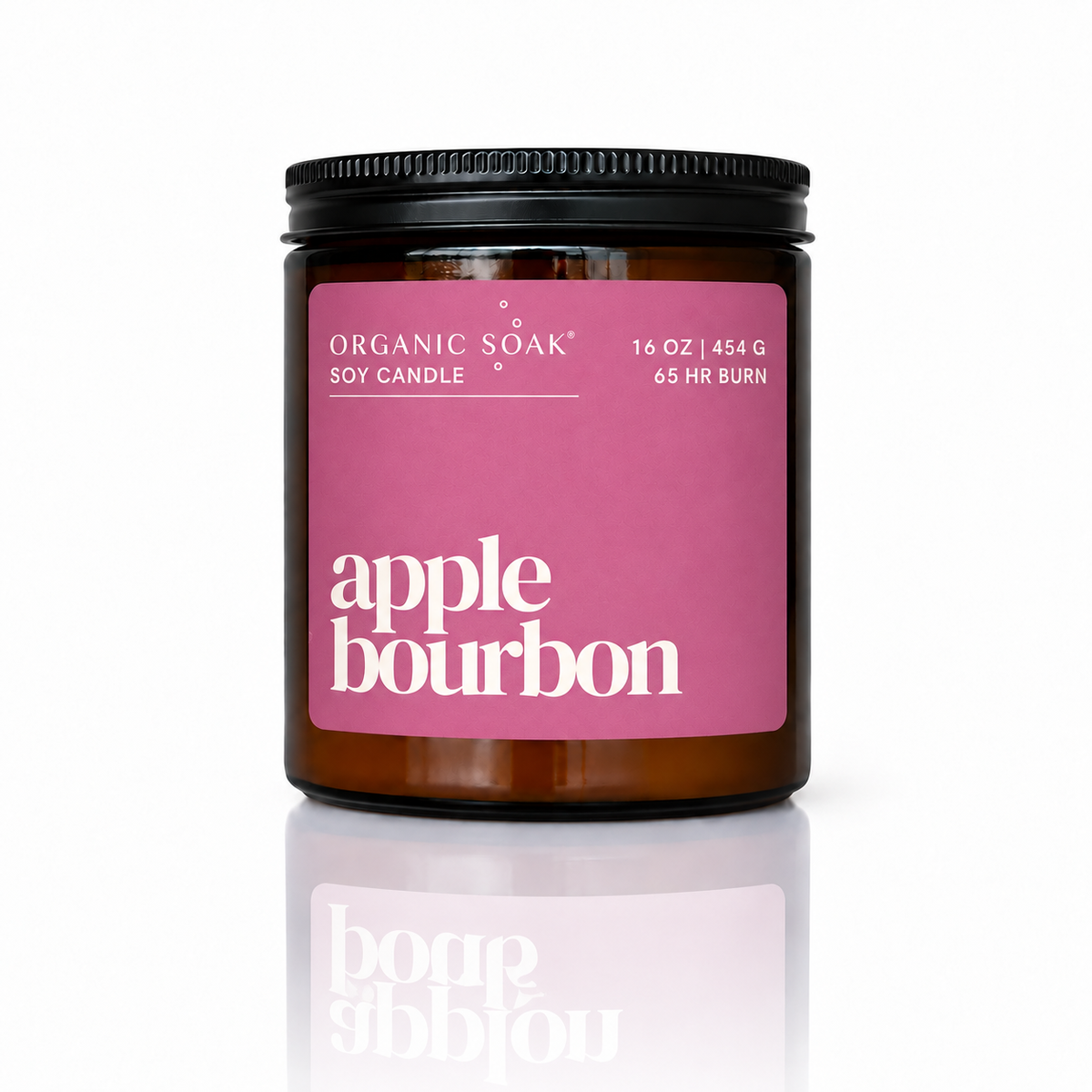 An Organic Soak soy candle in an amber glass jar with a black lid and a pink label reading &