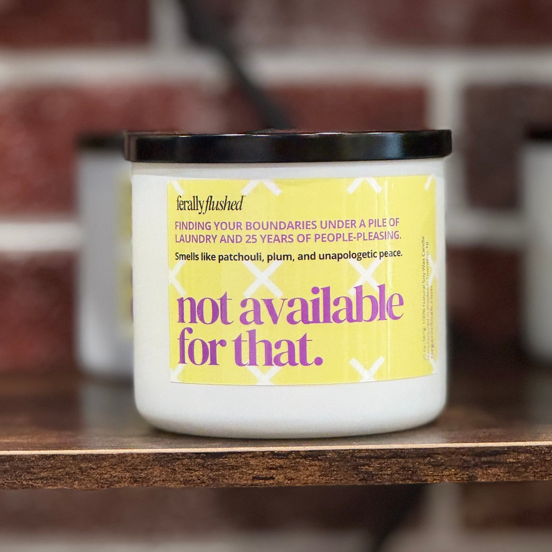 Candle with a humorous label on a wooden surface against a brick wall background