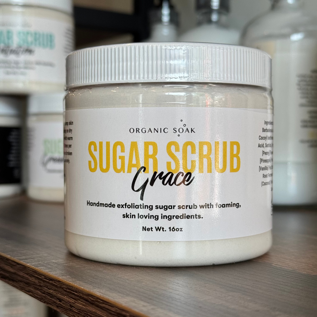 Jar of Organic Soak Sugar Scrub Grace on a shelf with other skincare products.