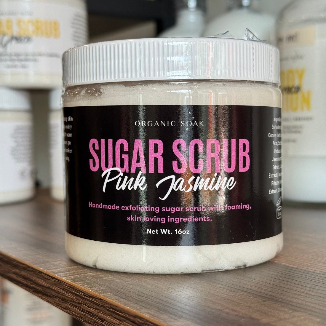 Jar of Organic Soak Pink Jasmine Sugar Scrub on a shelf with similar products in the background.