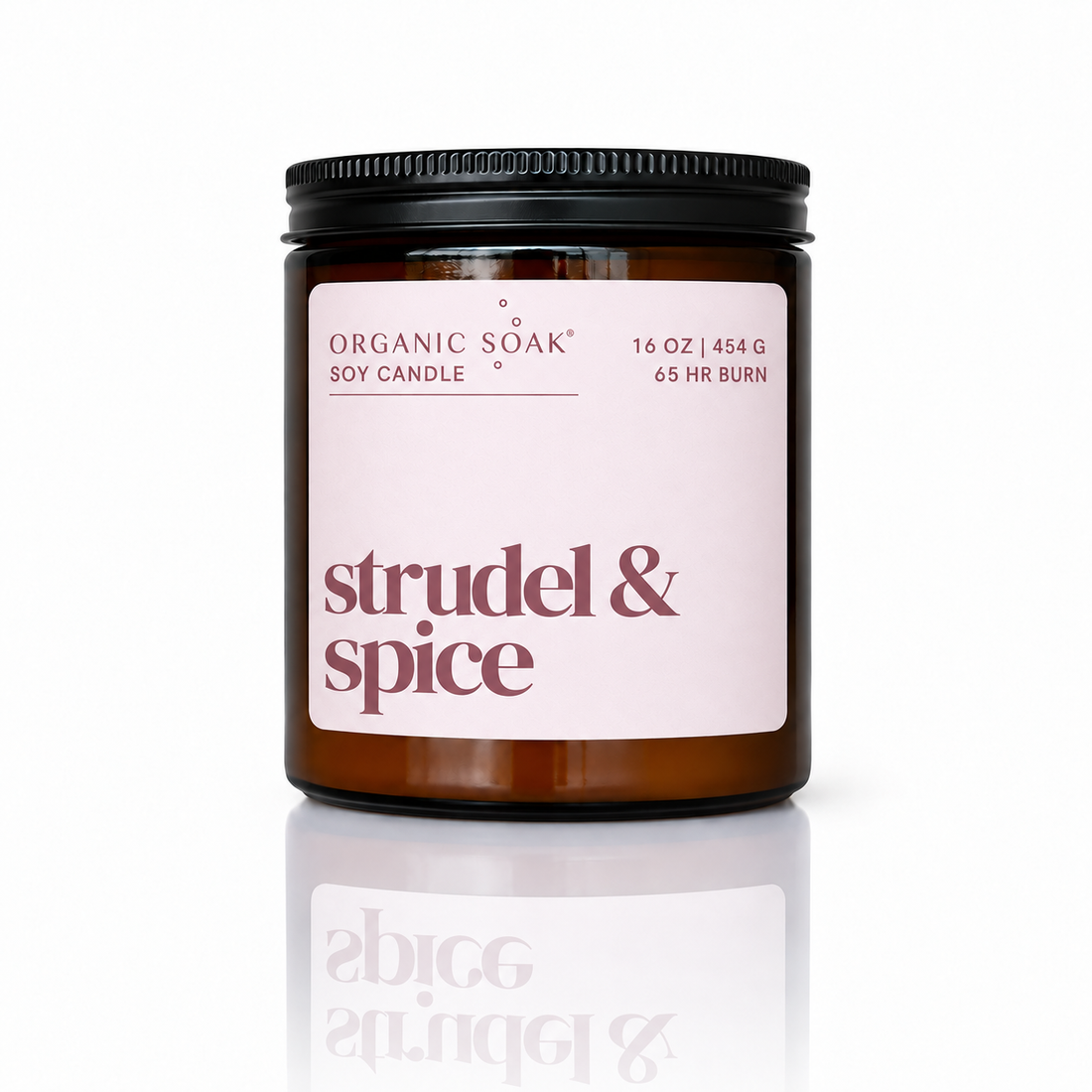 An amber glass jar candle with a black screw-top lid and a pale pink label reading &