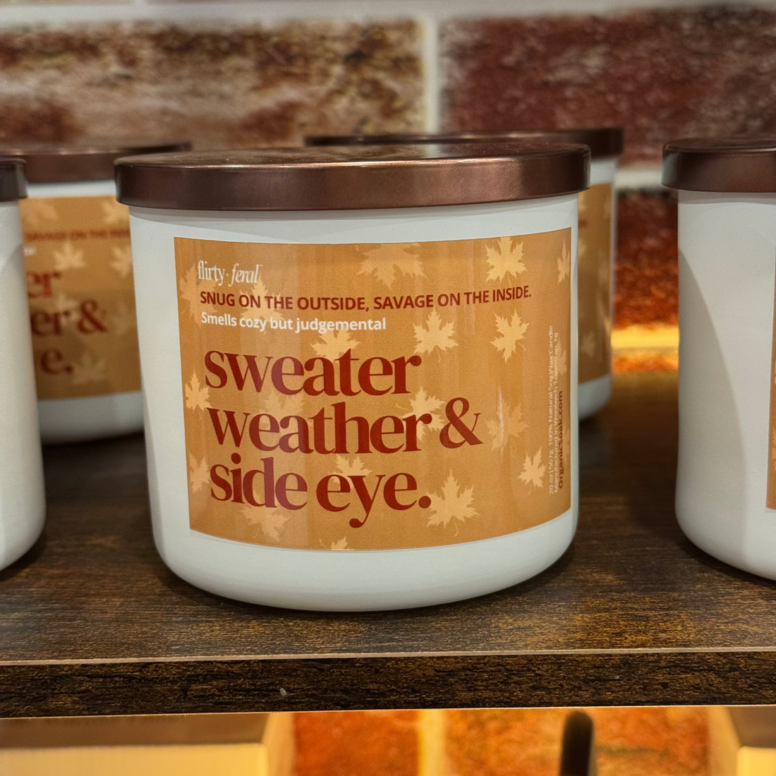 Candle with a humorous label on a wooden surface with a brick wall background